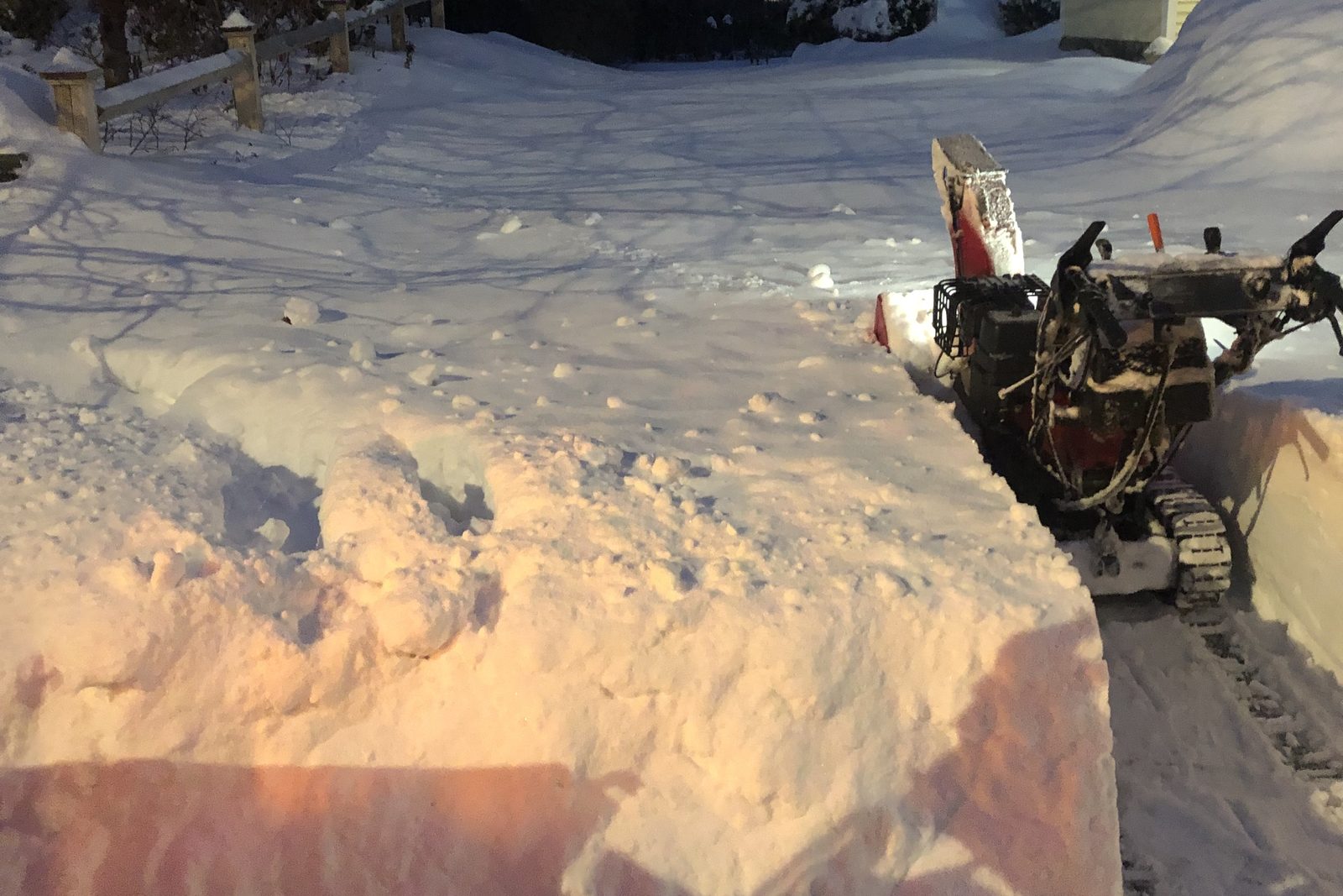 A residential driveway cut clean through deep snow by snowblower, with the snow banked to the side
